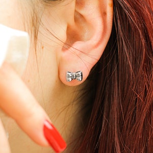 May include: A close-up of a person's ear with a small silver bow-shaped earring.