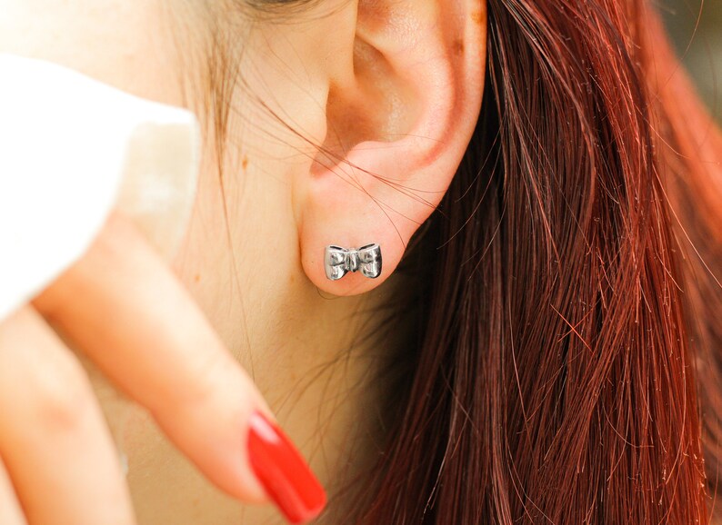 May include: A close-up of a person's ear with a small silver bow-shaped earring.