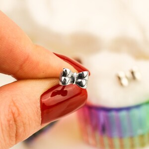 May include: A silver bow-shaped earring with a textured surface.