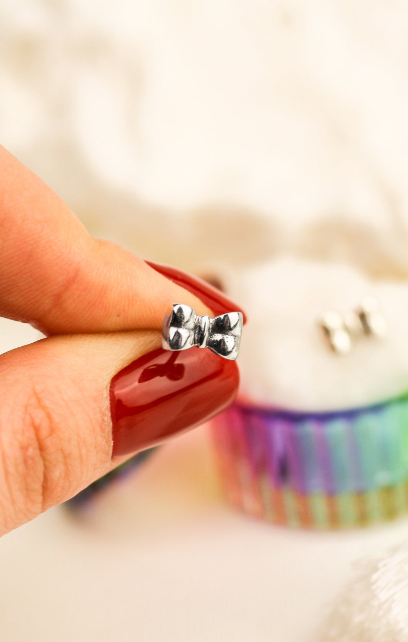 May include: A silver bow-shaped earring with a textured surface.