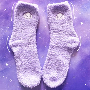 May include: A pair of fluffy lavender socks with a cute embroidered cartoon face on each sock.