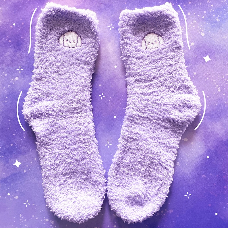 May include: A pair of fluffy lavender socks with a cute embroidered cartoon face on each sock.
