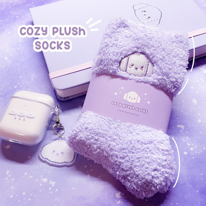 May include: Purple fluffy socks with a white embroidered dog on the front. The socks are packaged in a clear plastic bag with a white label that says "cozy plush socks" and "shortysycreeations".