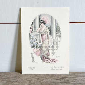 May include: A vintage illustration of a woman in a pink and white gown with a feathered hat. The woman is standing in a garden setting with a fan in her hand. The illustration is from "L'Album de Bal Hiver 1911-1912".