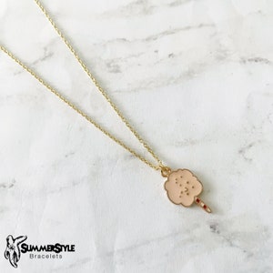 May include: A gold chain necklace with a pink cotton candy charm. The charm has a red and white stick.