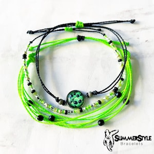 May include: A set of three friendship bracelets with green and black string, black beads, and a green alien charm. The bracelets are tied together in a knot.