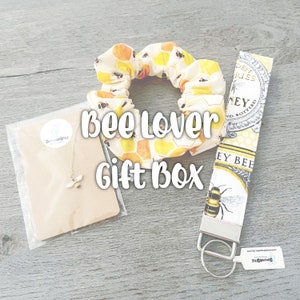 May include: A bee-themed gift box with a yellow and white scrunchie, a gold bee necklace, and a key chain with a bee design. The box includes the text "Bee Lover Gift Box".
