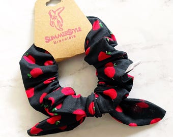 May include: Black scrunchie with red apple print. The scrunchie is tied in a bow and has a tag that says "SummerStyle Bracelets".