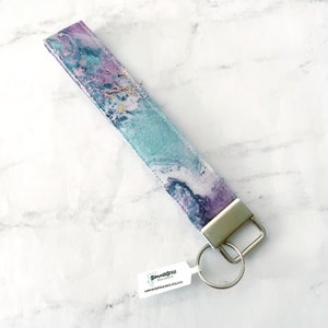 May include: A teal, purple, and white marbled fabric key chain with a silver key ring and a tag that reads "SummerStyle Bracelets summerstylebracelets.etsy.com".
