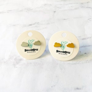 May include: Two pairs of cloud-shaped stud earrings. One pair is a light gray color and the other pair is a gold color. The earrings are displayed on white cards with the text "SUMMERSTYLE Bracelets".