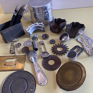 May include: A collection of vintage metal objects including a flour sifter, two can openers in a rectangular tin, a small bridge figurine, a spoon, a thimble, a star-shaped gear, a circular dial, a buckle, and various hardware components.