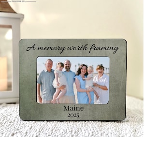 May include: A rectangular photo frame with a family photo inside. The frame is a muted green color with the words "A memory worth framing" in script at the top. The word "Maine" and the year "2025" are at the bottom.