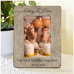 May include: A rectangular photo frame with a gray, textured finish. The frame holds a photo of two babies with cake on their faces, with the text "Nancy & Drew" at the top and "Our First Birthday Together 01/14/2026" at the bottom.