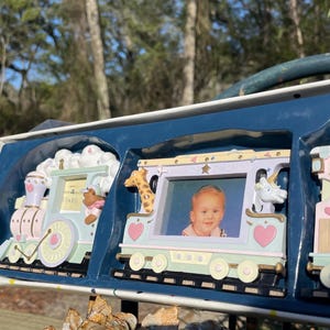 Op de afbeelding: Een set van drie pastelkleurige fotolijsten in de vorm van een trein. Elke lijst heeft een ander dieraccent, waaronder een giraf en een eenhoorn. De lijsten zijn ontworpen om kleine foto's te bevatten, perfect voor babyfoto's.
