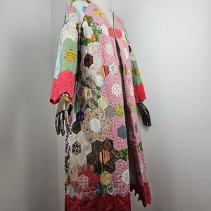 Può includere: Un cappotto lungo aperto sul davanti realizzato con un patchwork di vari esagoni di tessuto in diversi colori e motivi, tra cui quadretti vichy rossi, stampe floreali e texture a tinta unita. Il capo presenta maniche lunghe e un orlo smerlato rosso.