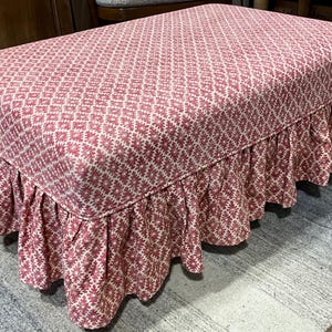 May include: A rectangular ottoman upholstered in a fabric featuring a repeating geometric diamond pattern in shades of red and white. The piece includes a gathered, ruffled skirt that extends from the base of the seat to the floor.