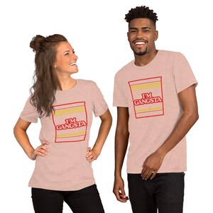 May include: Two people wearing pink t-shirts with a graphic of a ramen noodle cup that says "I'm Gangsta".