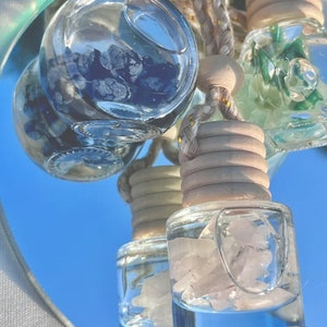 May include: Three glass car air fresheners with different colored crystals inside. The crystals are blue, green, and pink. The air fresheners are hanging from a string with a wooden bead.