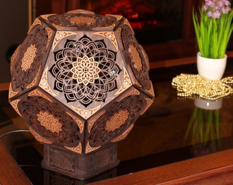 Może przedstawiać: Drewniana lampa o geometrycznym wzorze, z misternymi rzeźbami i ciemnobrązowym wykończeniem. Lampa stoi na stole ze szklanym blatem i drewnianym stelażem.