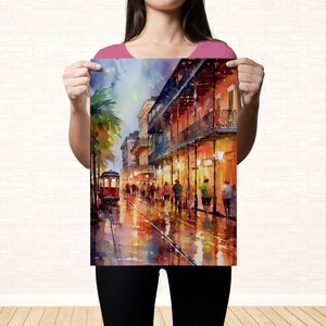 A woman holds up a colorful painting of a lively street scene with people, buildings, and a trolley car.