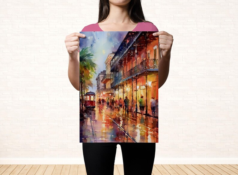 A woman holds up a colorful painting of a lively street scene with people, buildings, and a trolley car.