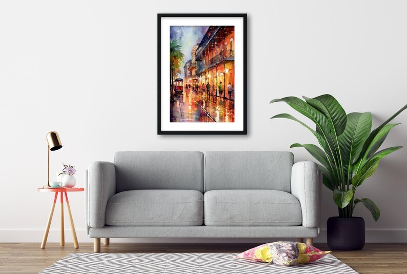 a gray sofa, a framed painting of a city street at night, a small table with a lamp, and a potted plant, all arranged in a living room setting.