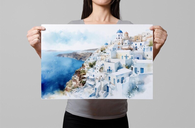 A woman holds up a framed print of a picturesque coastal town with white buildings and blue roofs, overlooking the ocean.
