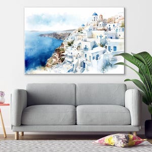 a living room with a gray sofa, a small table with a lamp, and a large painting of a coastal town with white buildings and blue roofs.