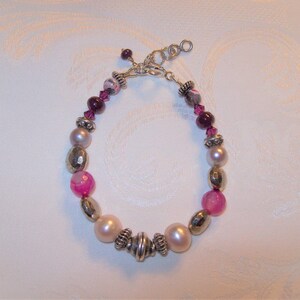 May include: A silver bracelet with pink, white, and gray beads. The bracelet has a silver clasp.