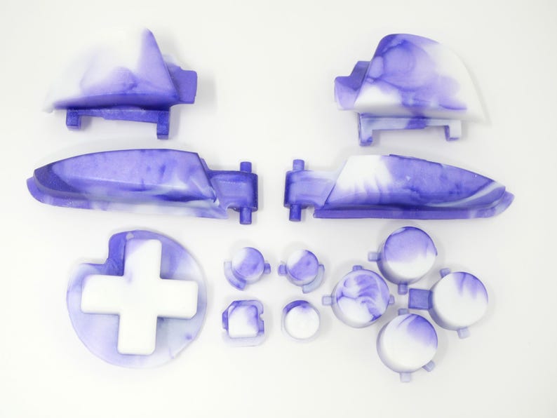 K&ouml;nnte beinhalten: Eine Sammlung von Ersatzteilen f&uuml;r Gamecontroller in einem marmorierten lila und wei&szlig;en Design. Das Set enth&auml;lt zwei Schultertasten, zwei Trigger, ein Steuerkreuz und verschiedene Knopfformen. Die Teile sind auf einer wei&szlig;en Oberfl&auml;che angeordnet.