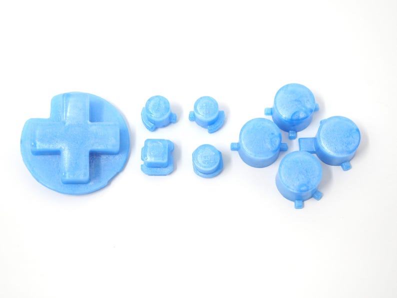 May include: A set of light blue gaming controller replacement buttons, including a D-pad, round buttons, and square buttons. The buttons are made of a solid, opaque material and are arranged on a white background.