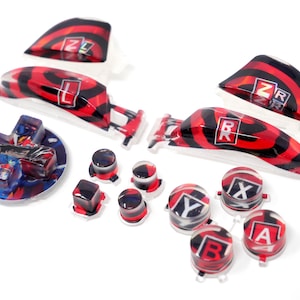 May include: A set of replacement gaming controller buttons and triggers featuring a glossy red and black swirl pattern. The buttons include a directional pad with character art, four action buttons labeled X, Y, B, A, and four shoulder triggers labeled ZL, ZR, L, and R.