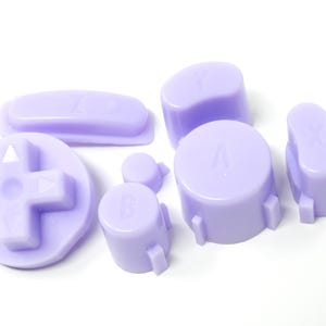 May include: A collection of light purple video game controller buttons, including a directional pad, oval, and circular buttons. The buttons are labeled with letters like A, B, X, Y, and Z.