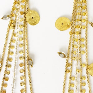 May include: Gold dangle earrings with multiple chains and small round discs. The chains are adorned with tiny beads and the discs have a hammered texture.
