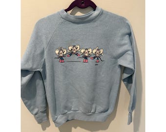 May include: A light blue crewneck sweatshirt featuring a graphic print of four cartoon mice dressed as ballerinas in pink tutus and ballet slippers. The mice are depicted in various dance poses across the centre of the chest area.