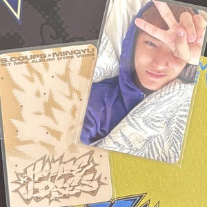 May include: A collection of photo cards featuring a person in a purple hoodie making a peace sign. The cards have text that reads "S.COUPS x MINGYU 1ST MINI ALBUM HYPE VIBES" and a graffiti-style design in shades of brown and yellow.