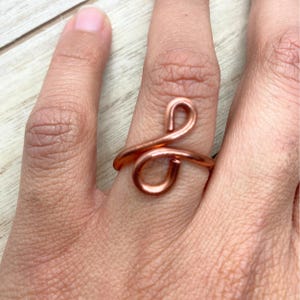 May include: A copper wire ring with a unique, twisted design. The ring is worn on a finger.