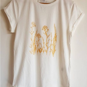 May include: White t-shirt with a yellow floral design. The design features a cluster of stylized flowers and leaves.
