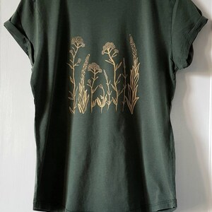 May include: A dark green t-shirt with a gold floral print. The print features a variety of stylized flowers and leaves.