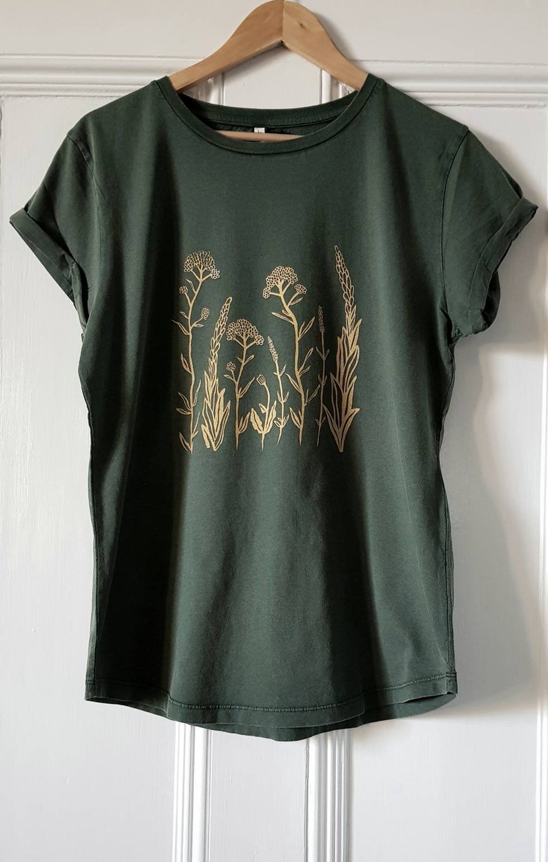May include: A dark green t-shirt with a gold floral print. The print features a variety of stylized flowers and leaves.