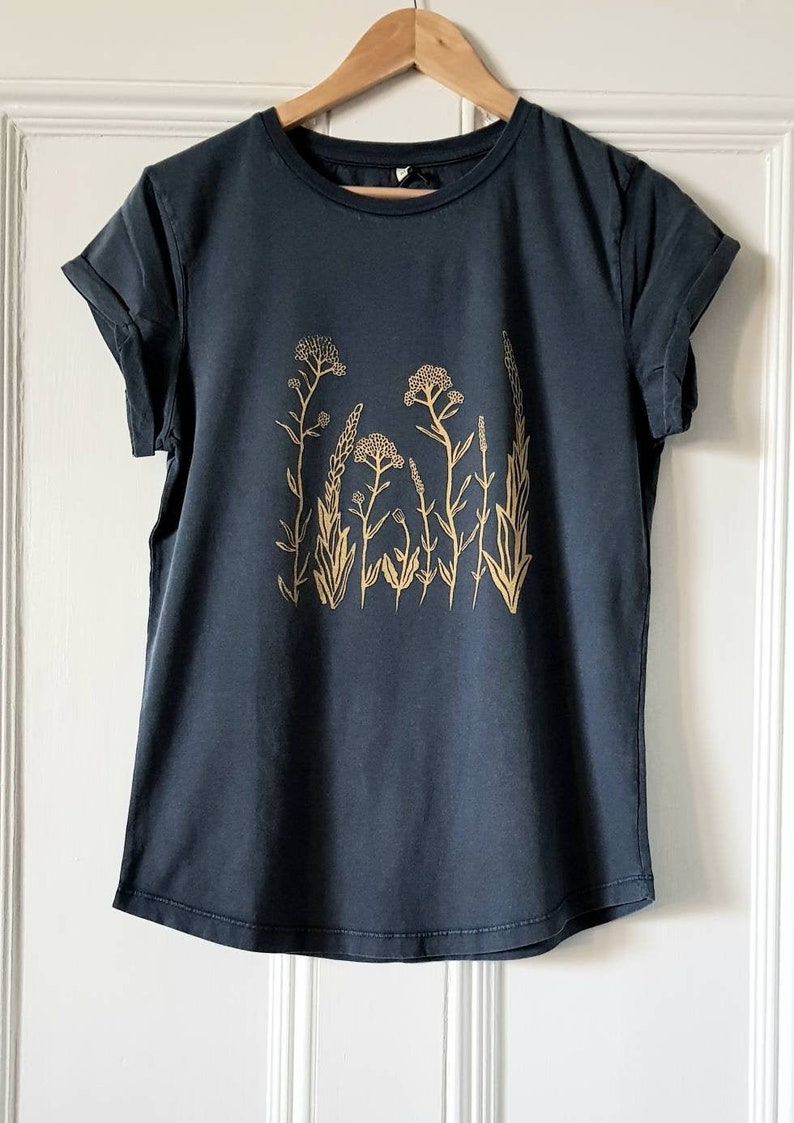 May include: A dark blue t-shirt with a gold floral print. The print features a cluster of stylized flowers and leaves.