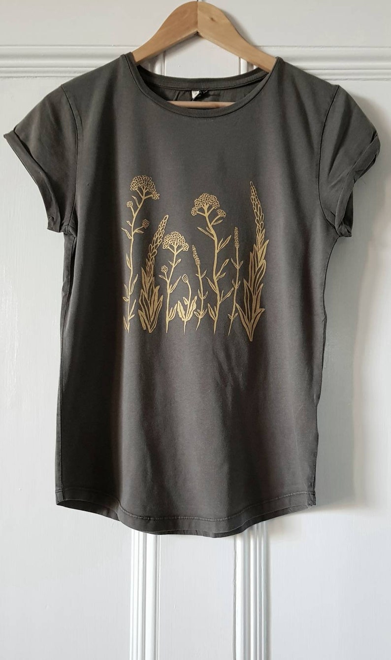 May include: A dark gray t-shirt with a gold floral print. The print features a variety of stylized flowers and leaves.