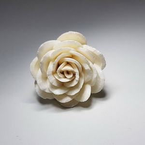 May include: A white, paper rose with multiple layers of petals. The rose is a decorative item and is made of a lightweight material.