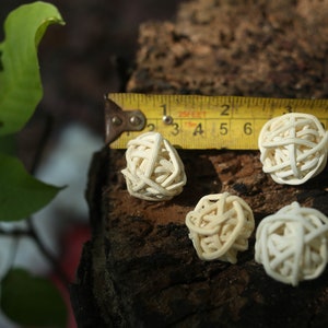 May include: Six white, woven, ball-shaped ornaments, measuring approximately 2 inches in diameter, are arranged on a piece of wood with a yellow measuring tape.