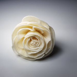 Pode incluir: Uma rosa branca de papel, com um design em camadas e plissado. A rosa é um item decorativo e é feita de um material macio e flexível.