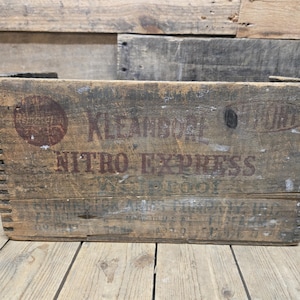 May include: A vintage wooden crate with the words "KLEANSBORO" and "NITRO EXPRESS" printed on the front. The crate is weathered and has a rustic appearance.