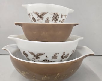 May include: A stack of four nesting mixing bowls with handles. Two bowls are white with brown graphic prints of eagles, roosters, and coffee grinders. The other two bowls are solid brown. The bowls are arranged in a vertical, alternating pattern.