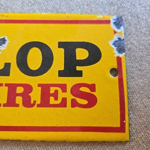 K&ouml;nnte beinhalten: Ein gelbes Vintage-Schild von Dunlop Tires mit schwarzer und roter Schrift. Das Schild hat einen roten Rand und weist Gebrauchsspuren auf, darunter abgeplatzte Farbe und ein kleines Loch.