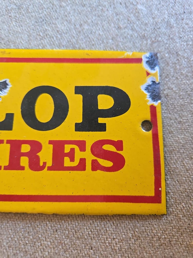 K&ouml;nnte beinhalten: Ein gelbes Vintage-Schild von Dunlop Tires mit schwarzer und roter Schrift. Das Schild hat einen roten Rand und weist Gebrauchsspuren auf, darunter abgeplatzte Farbe und ein kleines Loch.