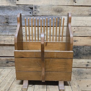 May include: A vintage wooden dish rack with a natural finish. The rack features a rectangular base, a central handle, and a series of vertical wooden dowels for holding plates. The design is simple and functional, showcasing the wood grain.